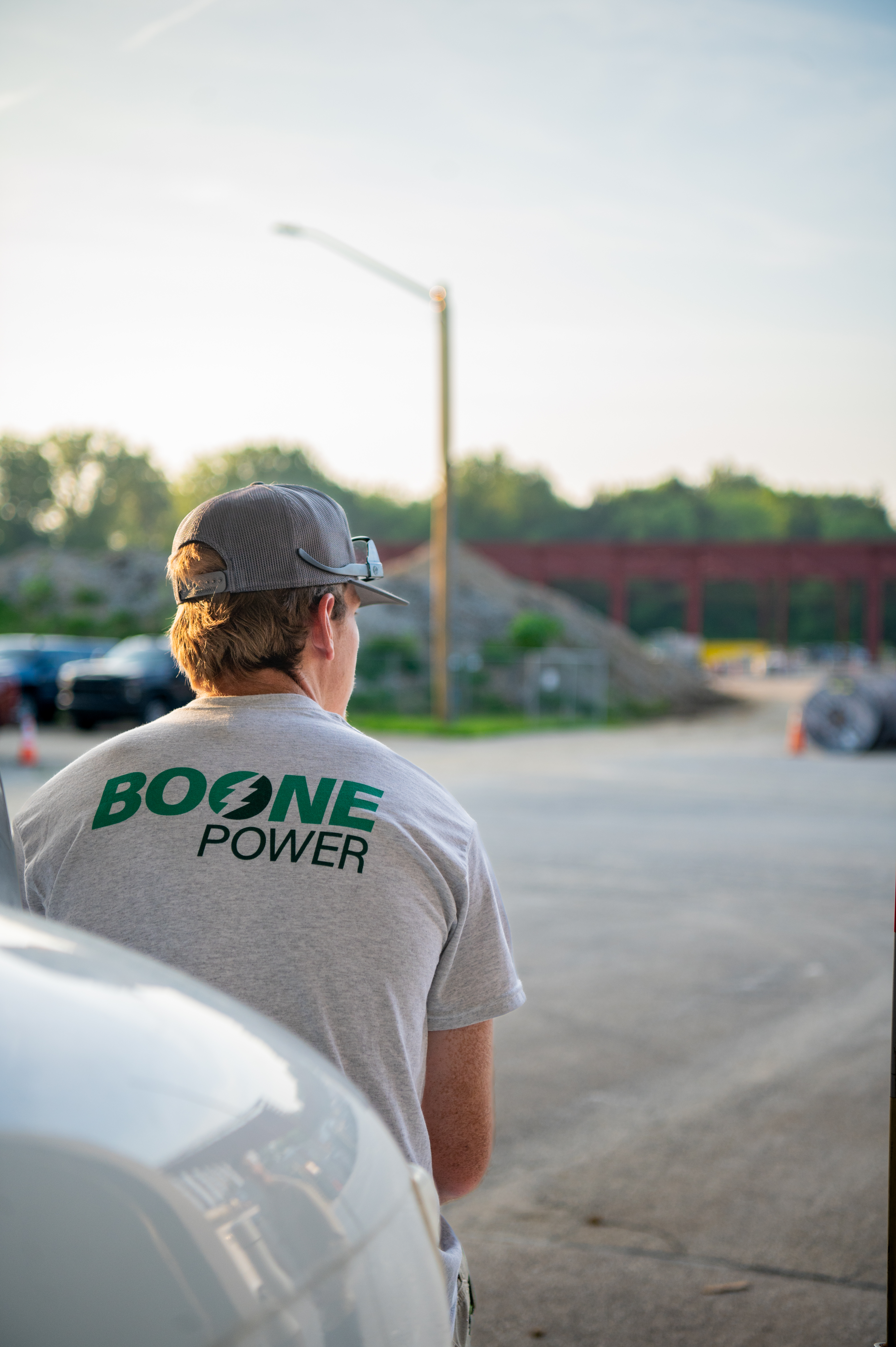 A Boone Power male employee sits on the front bumper of a utility truck wearing a branded shirt.