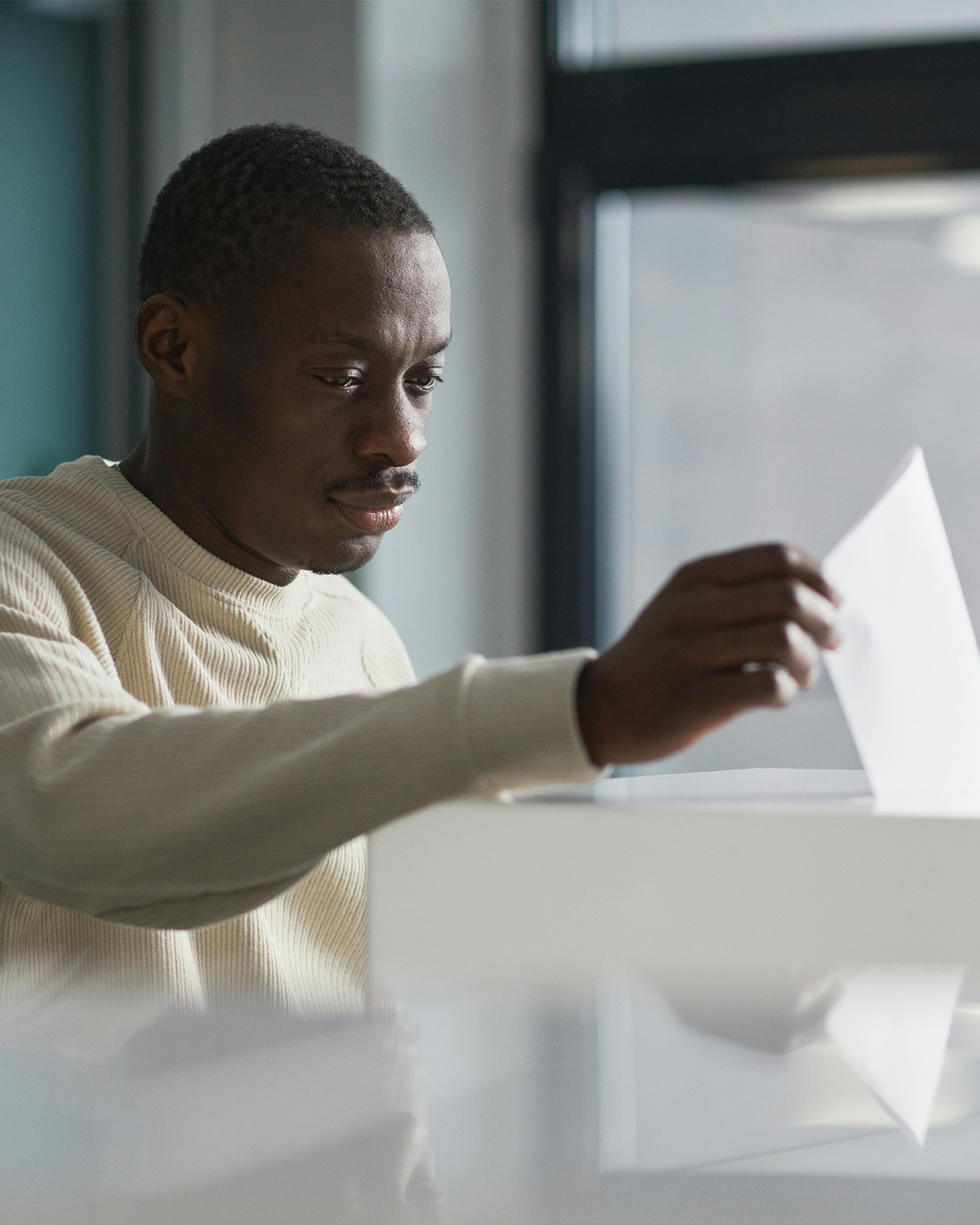A man in a yellow sweater deposits a ballot into a box.
