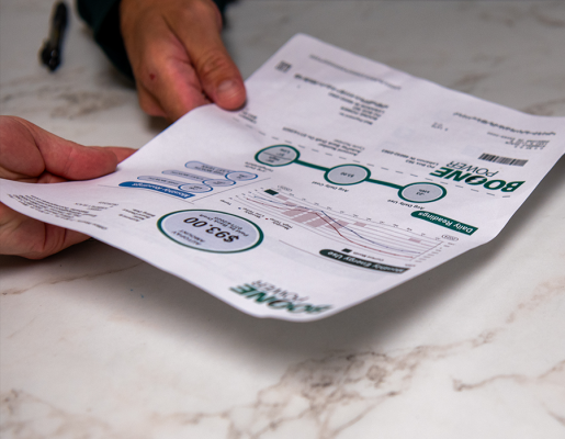 A man's hand passes a Boone Power bill to a female hand on a white marble-veined counter.